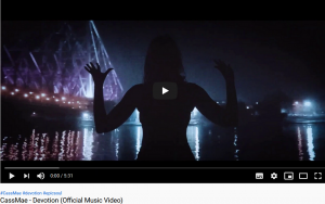 Startbild des offiziellen Videos "Devotion" von CassMae. Silhuette einer Frau im Dunklen vor einer Wasserfläche und Lichtern einer Brücke, sowie Bootslichter