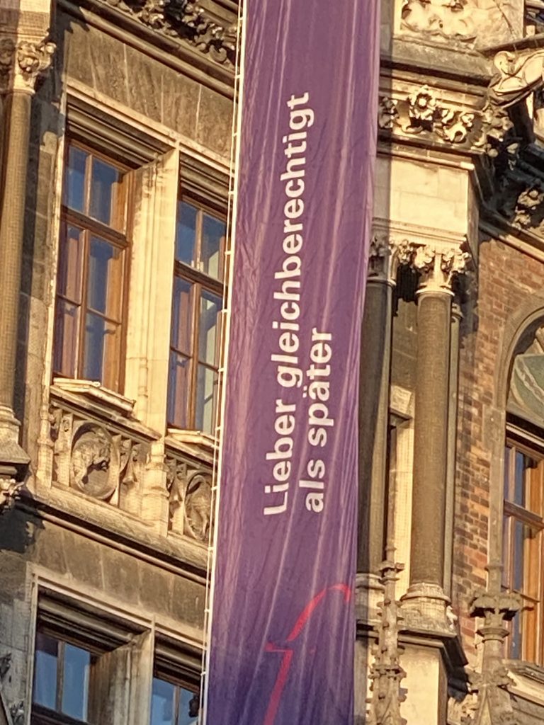 Vor dem Münchener Rathaus weht zum Weltfrauentag eine lilafarbene Fahre mit dem Slogan "Lieber gleichberechtigt als später"
