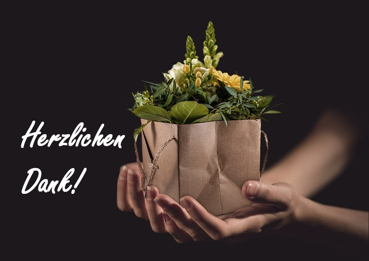 Vor dunklem Hintergrund reichen Frauenhände ein Blumengesteck aus grünen, gelben und weißen Blumen, das dekorativ in einer braunen Papiertüte sitzt. Links steht in weißer Schrift "Herzlichen Dank!"
